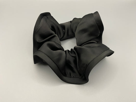 “The Rebecca Flower Scrunchie in Black, featuring a flower-shaped design made from durable and soft satin material. Measures 11 cm, perfect for creating voluminous and eye-catching hairdos. Chic and versatile, ideal for adding a touch of vintage elegance to any outfit.”