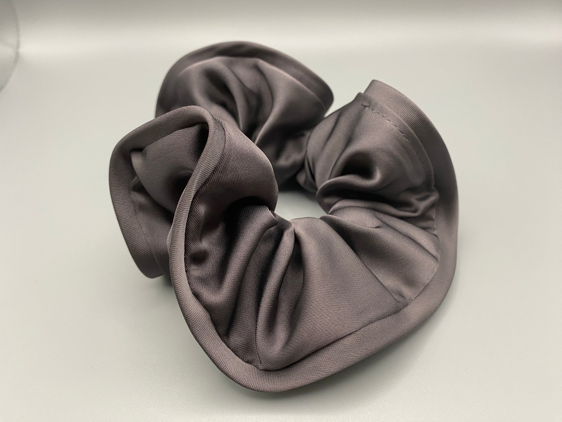 The Rebecca Flower Scrunchie in Grey, featuring a flower-shaped design made from durable and soft satin material. Measures 11 cm, perfect for creating voluminous and eye-catching hairdos. Chic and versatile, ideal for adding a touch of vintage elegance to any outfit.”