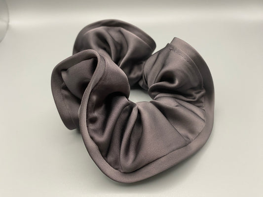 The Rebecca Flower Scrunchie in Grey, featuring a flower-shaped design made from durable and soft satin material. Measures 11 cm, perfect for creating voluminous and eye-catching hairdos. Chic and versatile, ideal for adding a touch of vintage elegance to any outfit.”