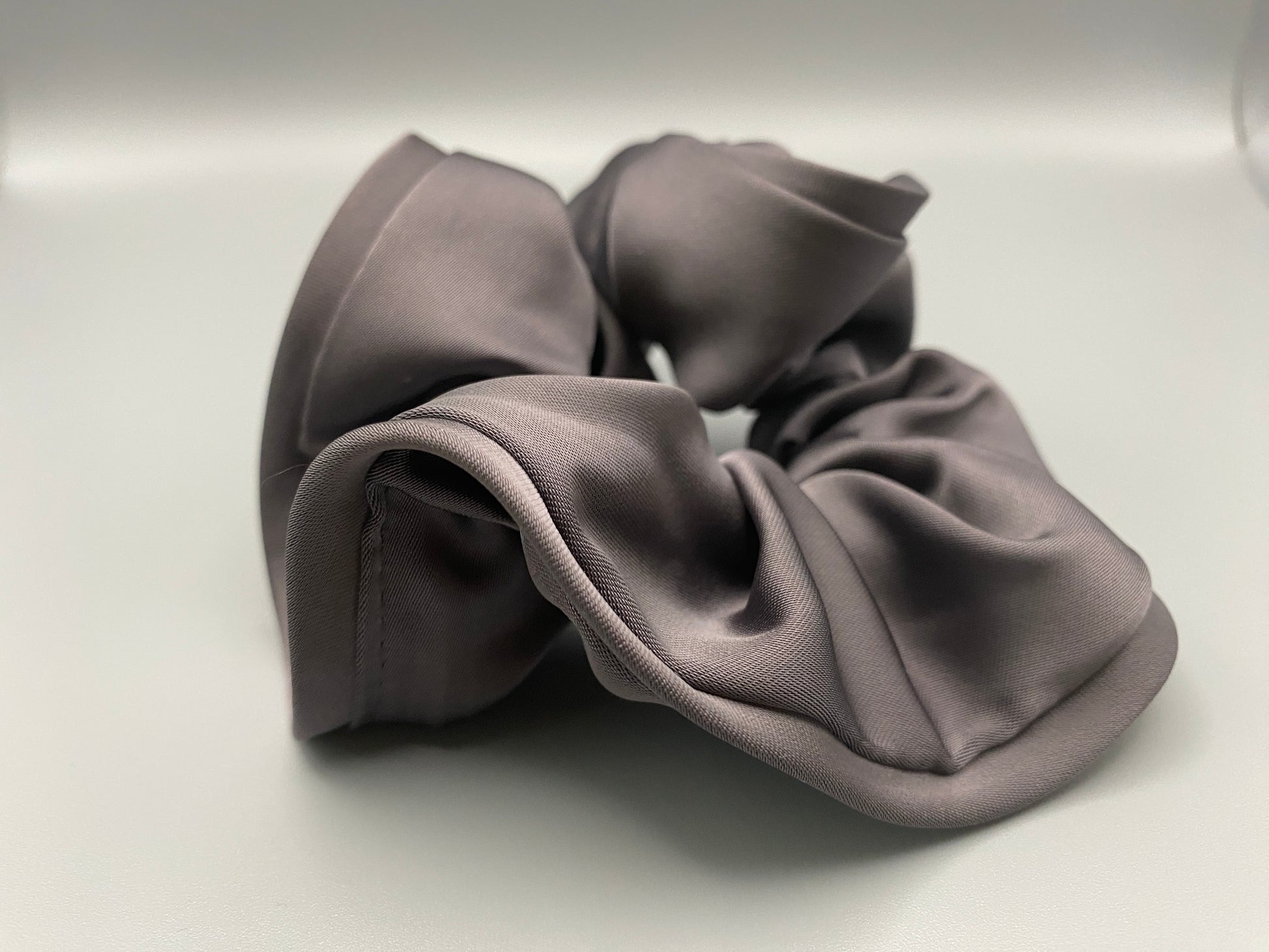 The Rebecca Flower Scrunchie in Grey, featuring a flower-shaped design made from durable and soft satin material. Measures 11 cm, perfect for creating voluminous and eye-catching hairdos. Chic and versatile, ideal for adding a touch of vintage elegance to any outfit.”