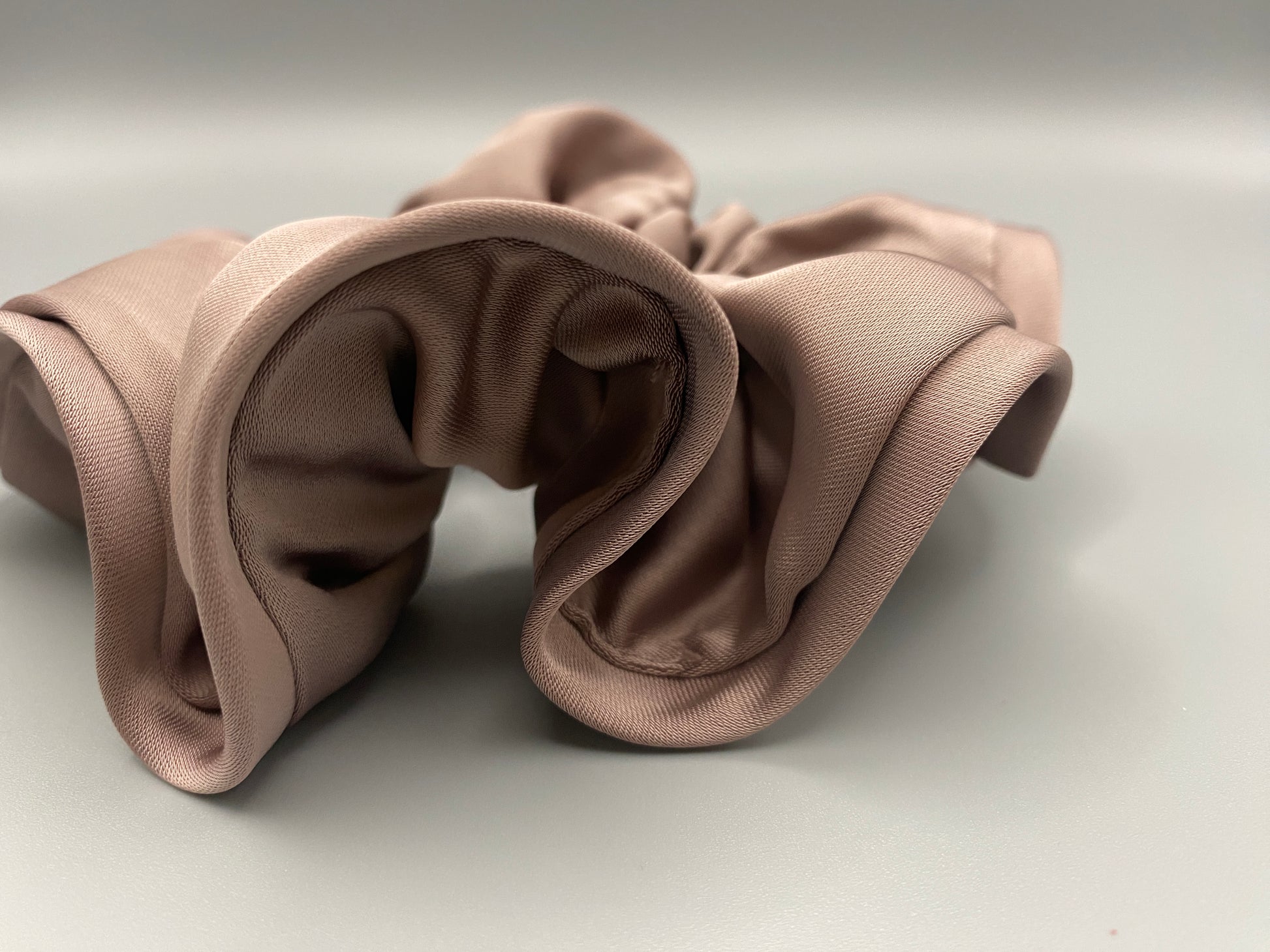 “The Rebecca Flower Scrunchie in Nude, featuring a flower-shaped design made from durable and soft satin material. Measures 11 cm, perfect for creating voluminous and eye-