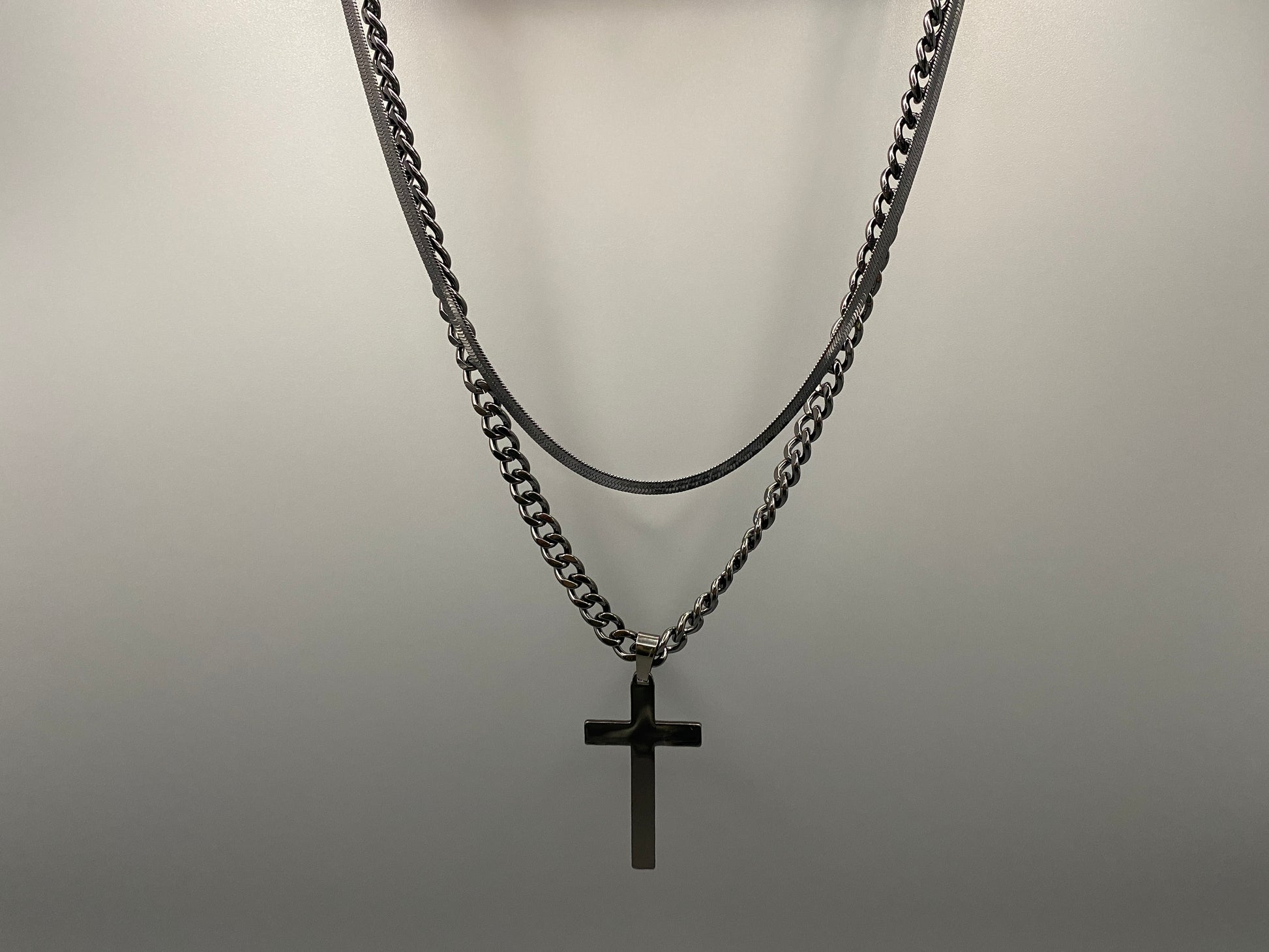 “Men’s Twin Chain Cross Necklace: A stylish black stainless steel necklace featuring a twin chain design with a silver-plated cross pendant. Perfect for teens and adults, this fine jewelry piece is unisex and measures 45 cm with a 5 cm extender.”