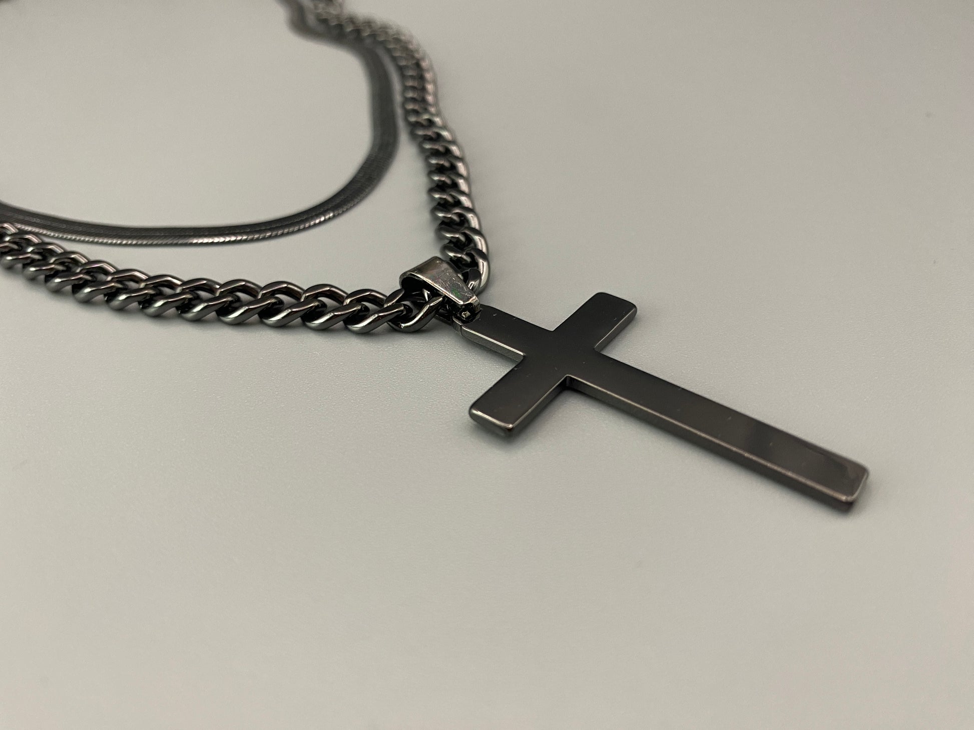 “Men’s Twin Chain Cross Necklace: A stylish black stainless steel necklace featuring a twin chain design with a silver-plated cross pendant. Perfect for teens and adults, this fine jewelry piece is unisex and measures 45 cm with a 5 cm extender.”