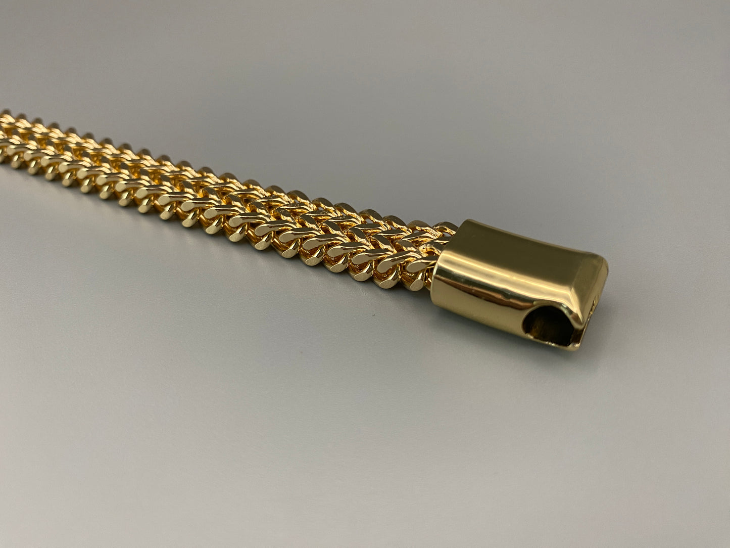 “A men’s bracelet with a chain and link design, made from shiny titanium steel. The bracelet features a geometric pattern and a smart magnet button clasp. It is available in silver, gold, and black colors, and measures 19-23 cm in length.”