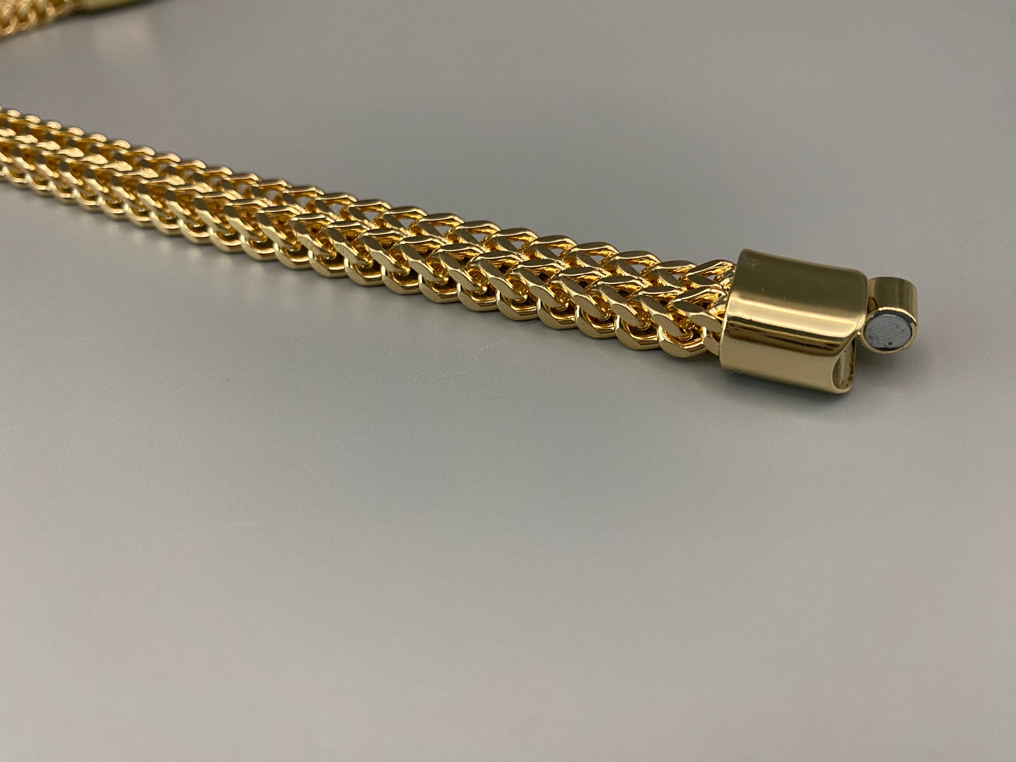 “A men’s bracelet with a chain and link design, made from shiny titanium steel. The bracelet features a geometric pattern and a smart magnet button clasp. It is available in silver, gold, and black colors, and measures 19-23 cm in length.”