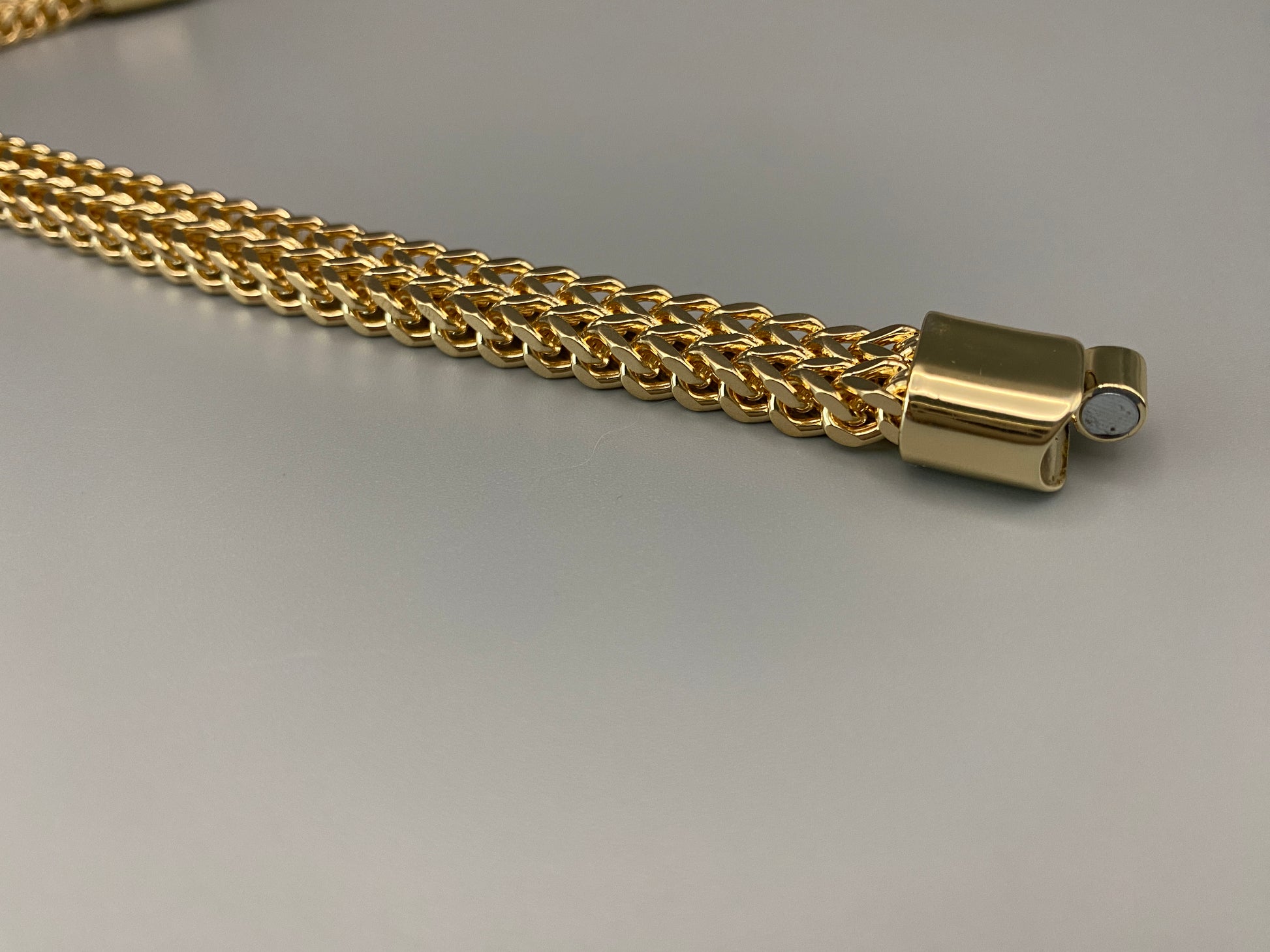 “A men’s bracelet with a chain and link design, made from shiny titanium steel. The bracelet features a geometric pattern and a smart magnet button clasp. It is available in silver, gold, and black colors, and measures 19-23 cm in length.”