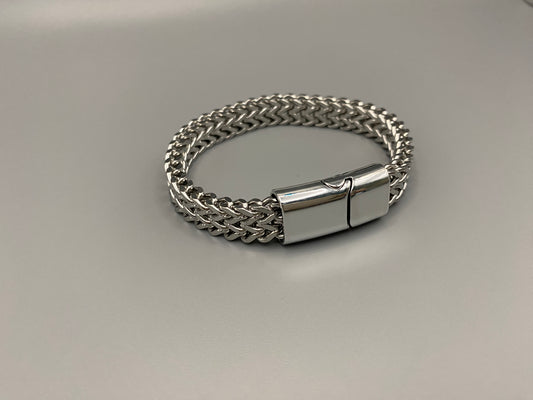 “A men’s bracelet with a chain and link design, made from shiny titanium steel. The bracelet features a geometric pattern and a smart magnet button clasp. It is available in silver, gold, and black colors, and measures 19-23 cm in length.”