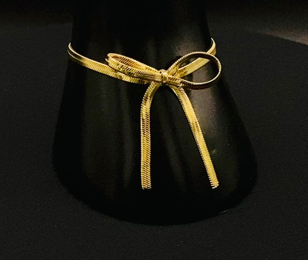 “Celest Angel Bow Bracelet in gold featuring a delicate bow design, made of stainless steel for durability and tarnish resistance. Measures 18 cm with a 3 cm extender for adjustable fit.”