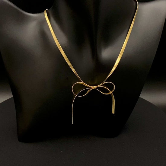 “Celest Angel Bow Pendant Chain in gold with a sophisticated bow pendant design. Made from durable stainless steel, tarnish-free. Measures 35 cm with a 5 cm extender for adjustable fit.”