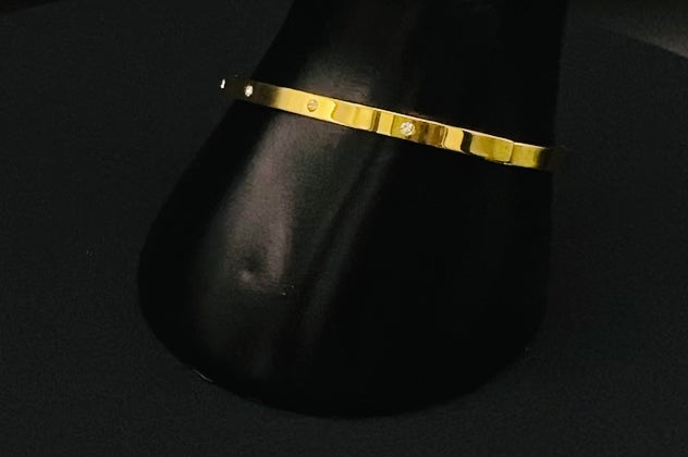 “Lucy Bangle in Gold with 18K gold plating, featuring a gemstone inlay for added elegance and sparkle. This durable bangle ensures long-lasting wear and resistance to tarnish. Its sophisticated design makes it perfect for both everyday wear and special occasions, adding a touch of glamour to any look.”