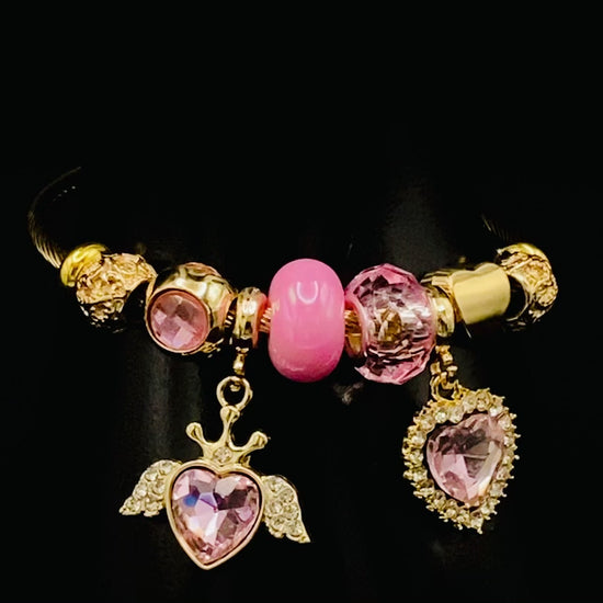 “Belle Pink Charm Bracelet with gold-plated finish, featuring heart-cut crystals and rhinestones. Made from durable stainless steel with playful charms and micro insert inlay technology.”