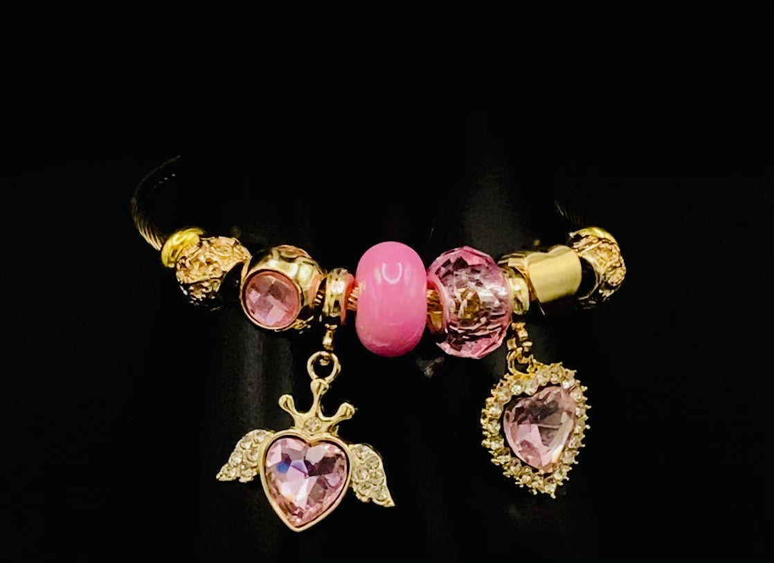 “Belle Pink Charm Bracelet with gold-plated finish, featuring heart-cut crystals and rhinestones. Made from durable stainless steel with playful charms and micro insert inlay technology.”