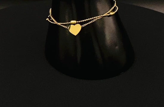 “Cora Twin Chain Heart and Bead Bracelet in gold, featuring a romantic twin chain design with heart and bead accents. 18K gold plated, made from durable titanium steel with PVD plating. Measures 17 cm with a 3 cm extender for adjustable fit.”