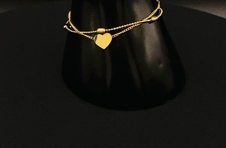 “Cora Twin Chain Heart and Bead Bracelet in gold, featuring a romantic twin chain design with heart and bead accents. 18K gold plated, made from durable titanium steel with PVD plating. Measures 17 cm with a 3 cm extender for adjustable fit.”