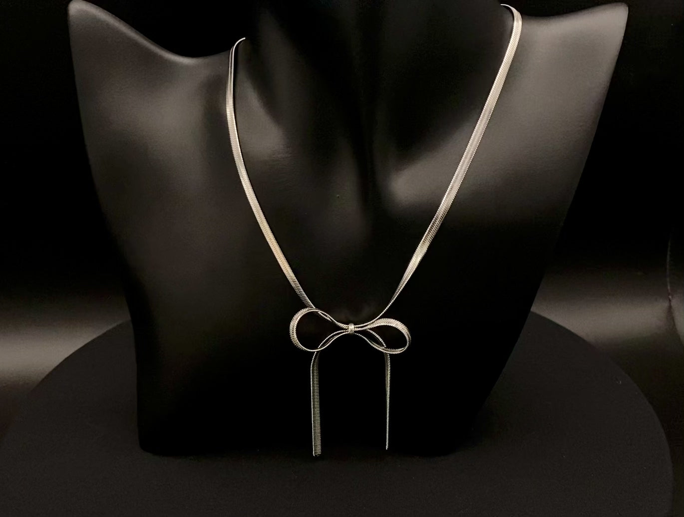 “Celest Angel Bow Pendant Chain in silver with a sophisticated bow pendant design. Made from durable stainless steel, tarnish-free. Measures 35 cm with a 5 cm extender for adjustable fit.”