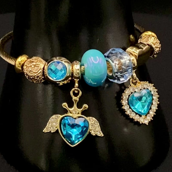 “Belle Blue Charm Bracelet with gold-plated finish, featuring heart-cut crystals and rhinestones. Made from durable stainless steel with playful charms and micro insert inlay technology.”