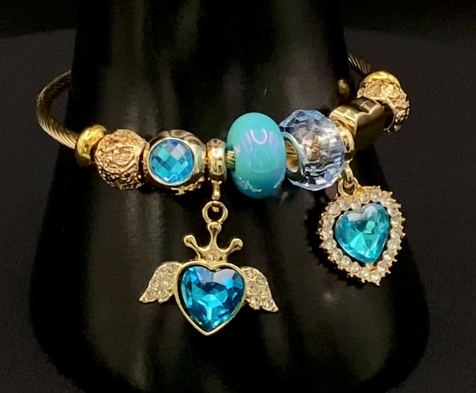 “Belle Blue Charm Bracelet with gold-plated finish, featuring heart-cut crystals and rhinestones. Made from durable stainless steel with playful charms and micro insert inlay technology.”