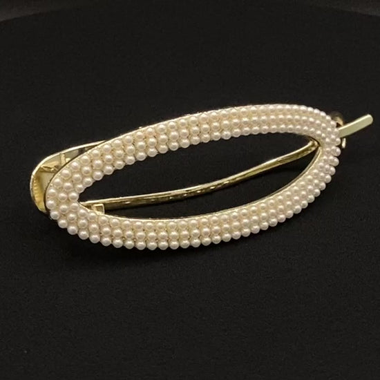  “GlitzGrip hair accessory with a hollow oval design, adorned with pearl inlayed gems and a gold finish, measuring 9.5 cm in length for a secure hold.”
