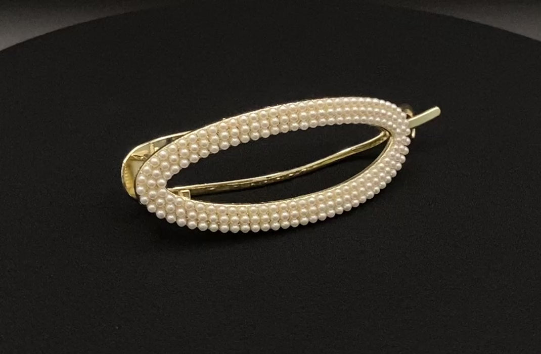  “GlitzGrip hair accessory with a hollow oval design, adorned with pearl inlayed gems and a gold finish, measuring 9.5 cm in length for a secure hold.”
