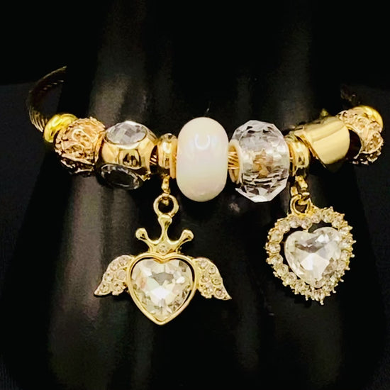 “Belle White Charm Bracelet with gold-plated finish, featuring heart-cut crystals and rhinestones. Made from durable stainless steel with playful charms and micro insert inlay technology.”
