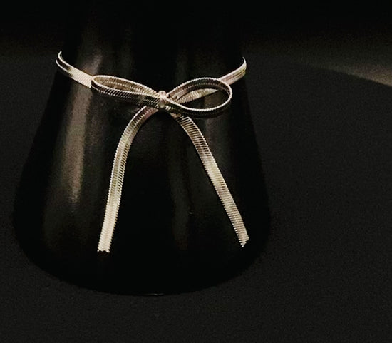 “Celest Angel Bow Bracelet in Silver featuring a delicate bow design, made of stainless steel for durability and tarnish resistance. Measures 18 cm with a 3 cm extender for adjustable fit.”