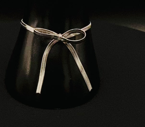 “Celest Angel Bow Bracelet in Silver featuring a delicate bow design, made of stainless steel for durability and tarnish resistance. Measures 18 cm with a 3 cm extender for adjustable fit.”